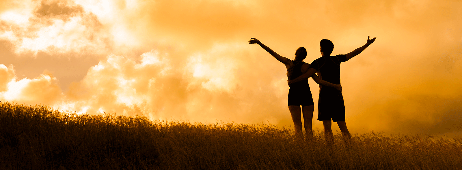 Couple standing in grass looking up at bright sky