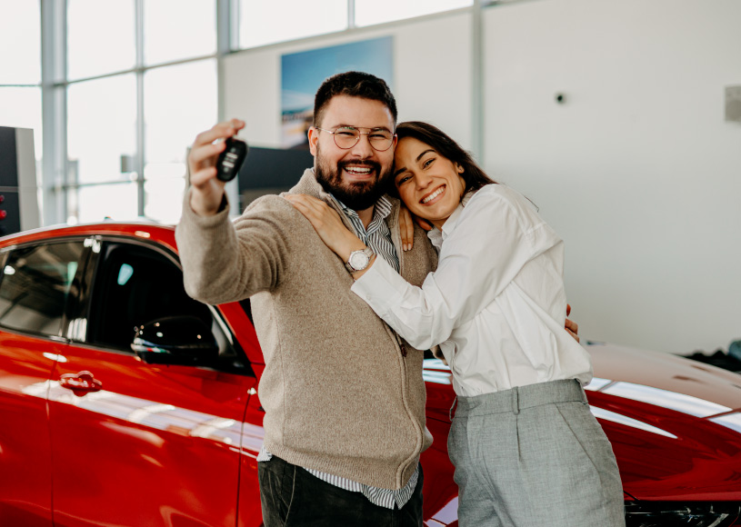 couple holding keys in front of car