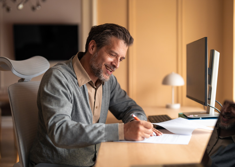 person writing on paper in front of computer