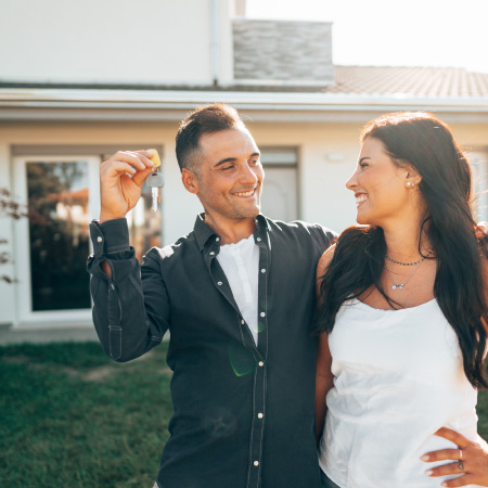 couple holding key in front of home